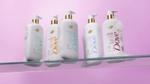 Cinco produtos da linha de sabonetes líquidos enriquecidos com MicroMoisture da Dove. Os recipientes são brancos com detalhes dourados e marca colorida, fotografadas contra um fundo lilás.